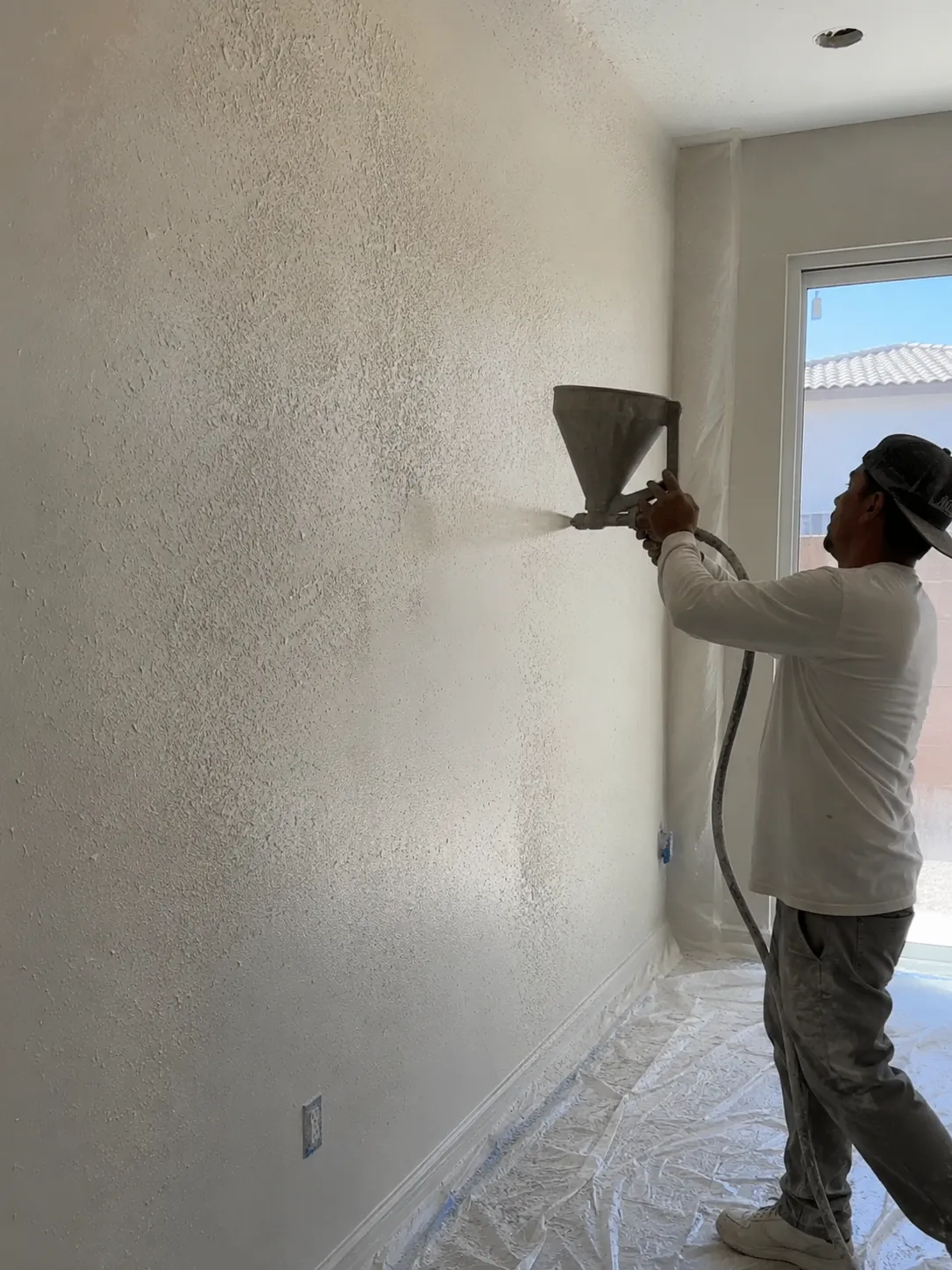 Worker spraying knockdown texture onto a wall in a Spring Valley home