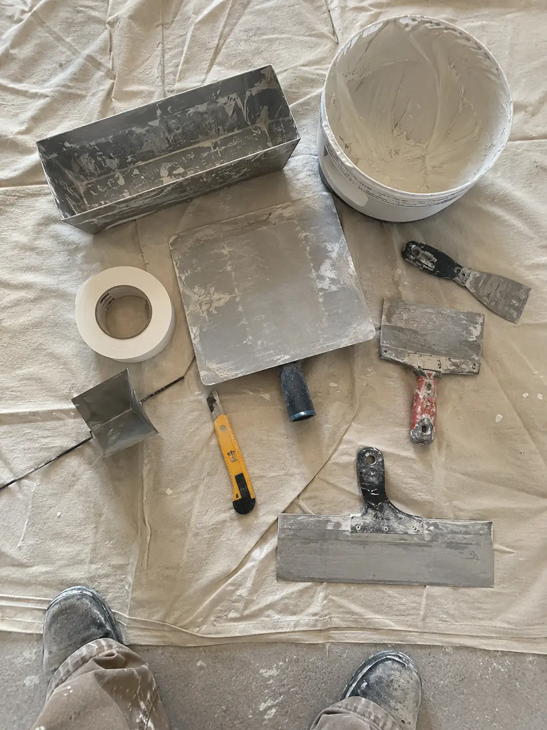 Drywall finishing tools laid out on a drop cloth