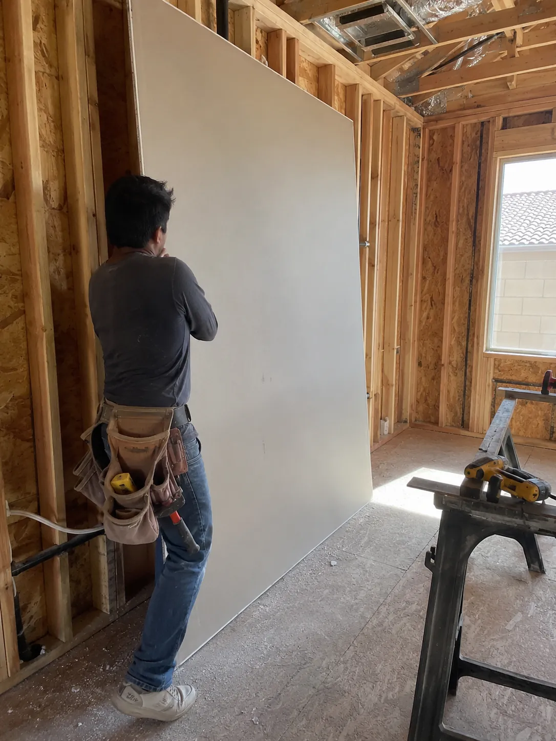 Installer hanging a sheet of drywall on wall framing in a Spring Valley home